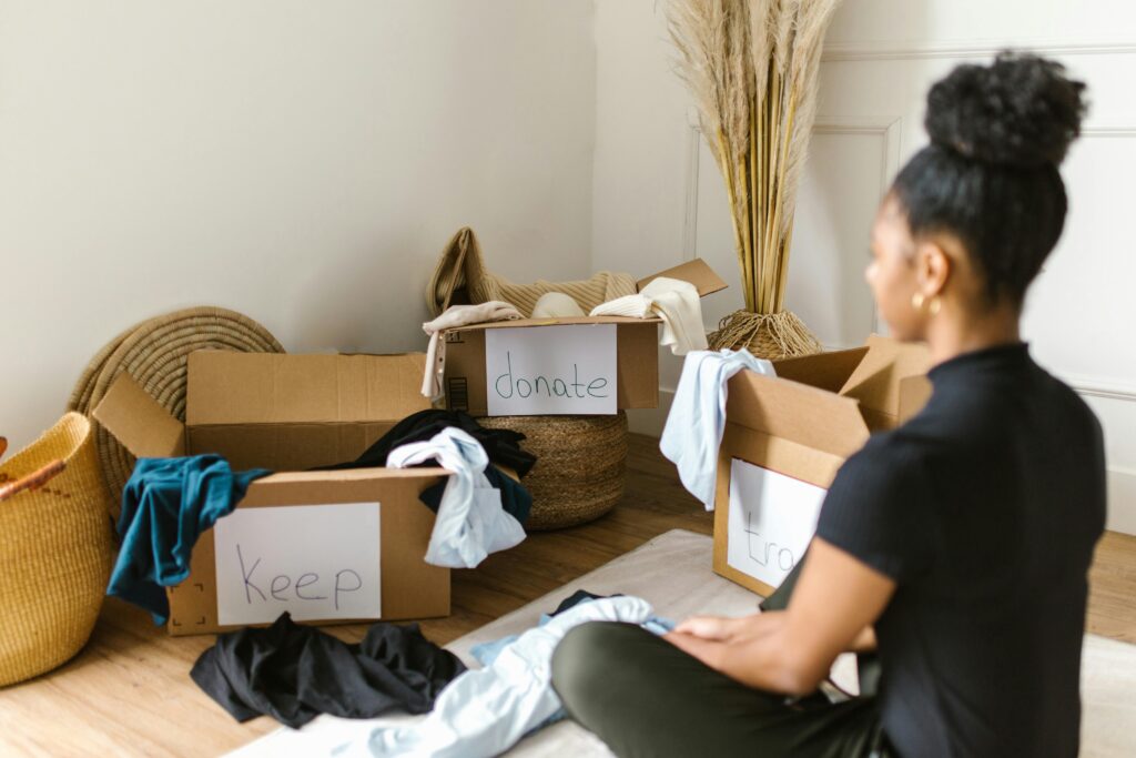 A woman sorts clothes into labeled boxes for keep, donate, and trash to decide what tokeep and what to let go before a move.