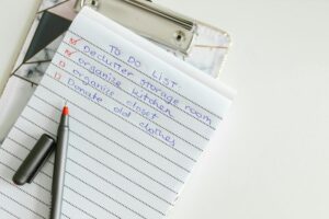 A handwritten to-do list on a clipboard with tasks to declutter, organize, and donateclothes before a move.