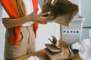 Close-up of a person organizing paper bags for recycling next to a bin labeled paper.